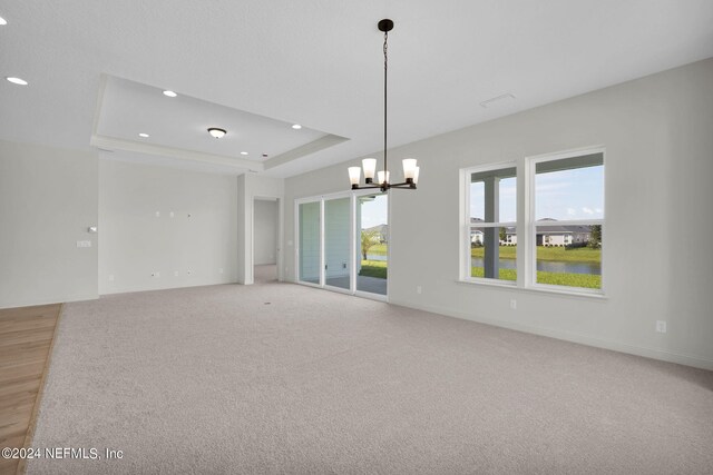 empty room featuring an inviting chandelier, a tray ceiling, and carpet flooring