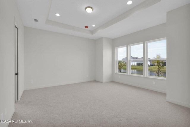 spare room with a tray ceiling, light colored carpet, and a water view