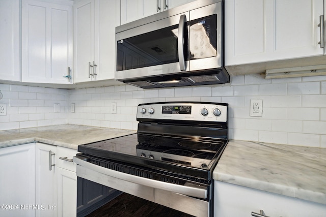 kitchen with light stone countertops, white cabinetry, appliances with stainless steel finishes, and backsplash