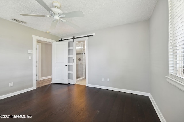 unfurnished bedroom featuring dark wood-type flooring, ceiling fan, connected bathroom, a textured ceiling, and a barn door