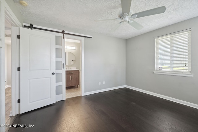 unfurnished bedroom featuring a barn door, connected bathroom, a textured ceiling, and dark hardwood / wood-style flooring