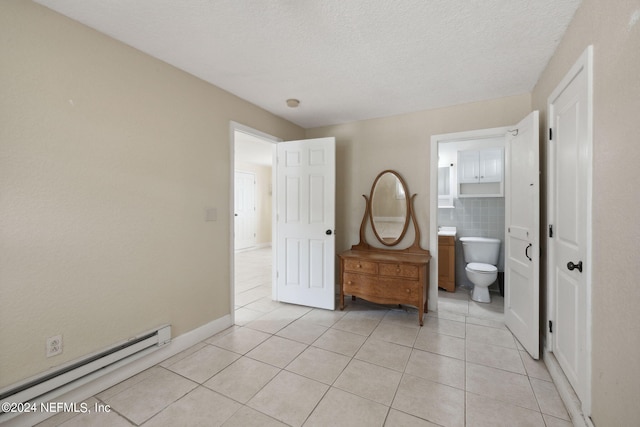 tiled bedroom featuring baseboard heating, ensuite bath, and a textured ceiling