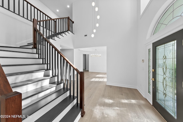 entrance foyer with an inviting chandelier, light hardwood / wood-style flooring, and a towering ceiling