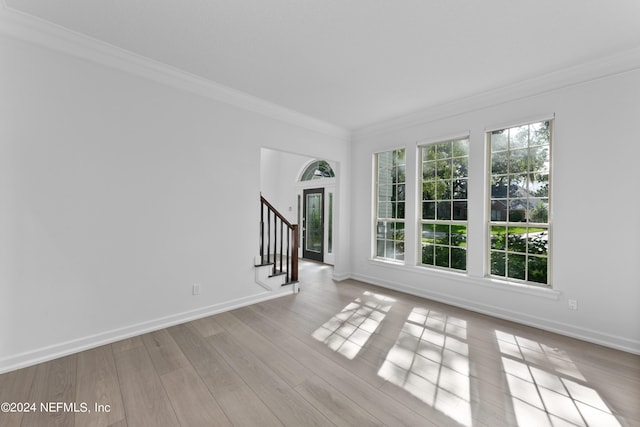 empty room featuring a wealth of natural light, crown molding, and light wood-type flooring