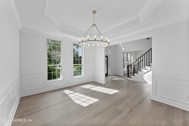 unfurnished dining area with crown molding, a notable chandelier, a tray ceiling, and light hardwood / wood-style floors