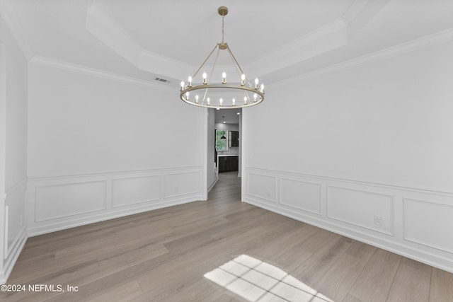 unfurnished dining area featuring hardwood / wood-style flooring, ornamental molding, a chandelier, and a raised ceiling