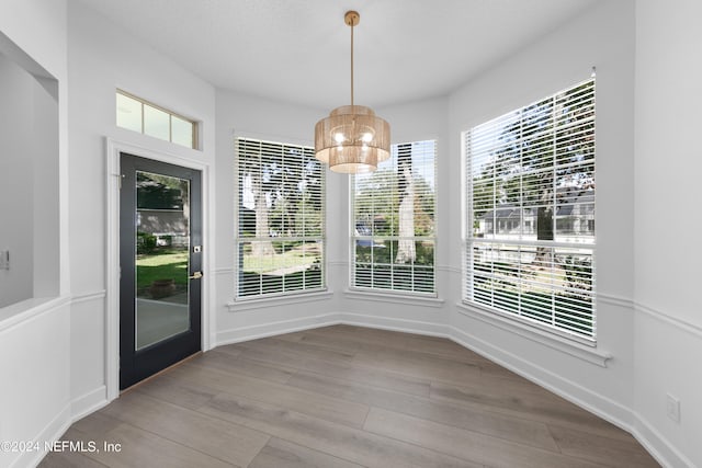 unfurnished dining area with hardwood / wood-style flooring, a healthy amount of sunlight, and an inviting chandelier