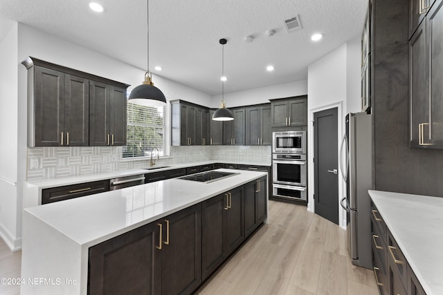 kitchen featuring appliances with stainless steel finishes, light wood-type flooring, sink, decorative light fixtures, and a center island