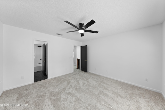 unfurnished bedroom featuring ensuite bathroom, a spacious closet, a textured ceiling, ceiling fan, and light carpet