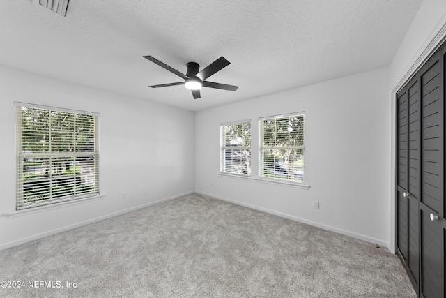 unfurnished bedroom featuring a textured ceiling, light colored carpet, a closet, and ceiling fan