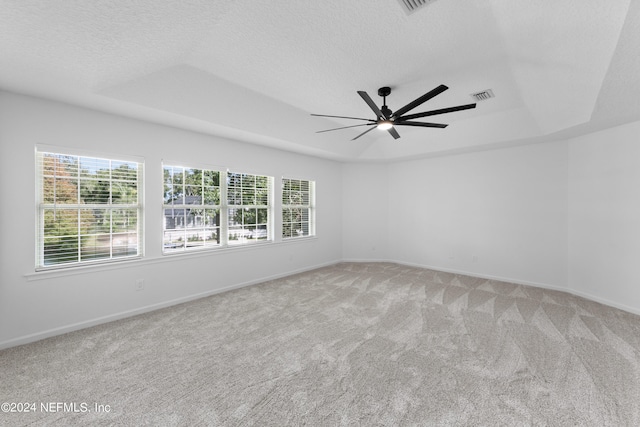 unfurnished room featuring ceiling fan, a textured ceiling, a tray ceiling, and light colored carpet