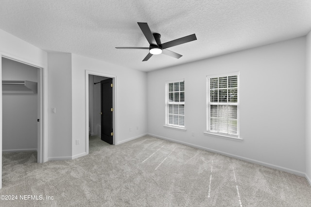 unfurnished bedroom with ceiling fan, a textured ceiling, a spacious closet, a closet, and light colored carpet