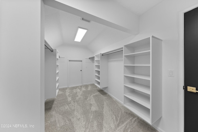 walk in closet featuring light carpet, a barn door, and vaulted ceiling