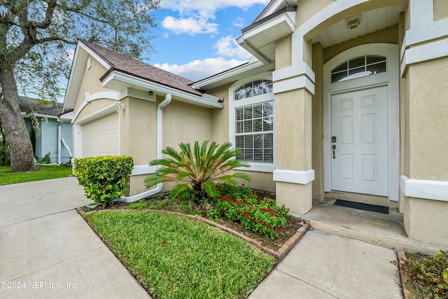 view of exterior entry featuring driveway, a garage, and stucco siding