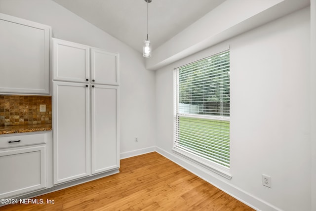 unfurnished dining area featuring light wood-style floors, baseboards, and vaulted ceiling