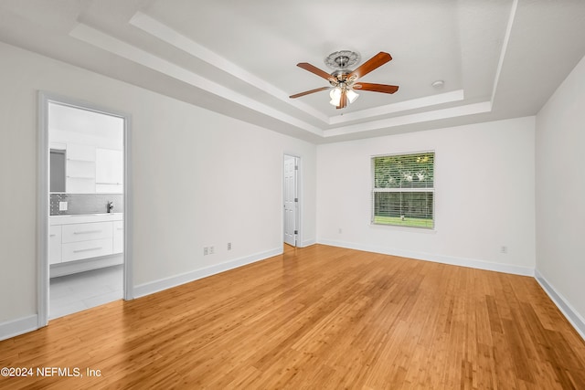 empty room featuring light hardwood / wood-style floors, a raised ceiling, and ceiling fan