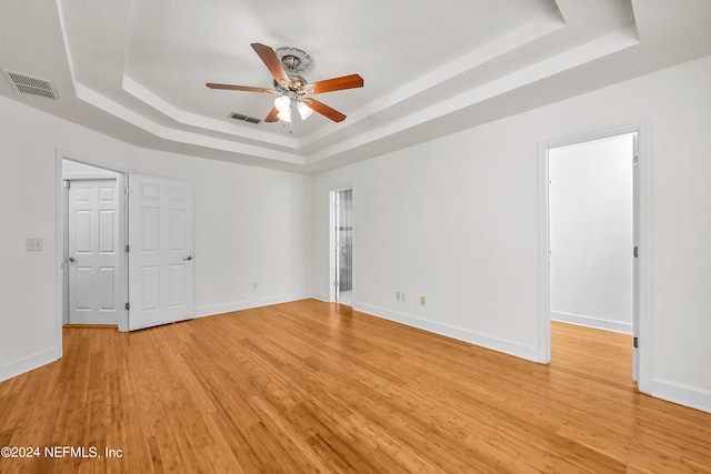 unfurnished room featuring a tray ceiling, light wood-style floors, ceiling fan, and visible vents