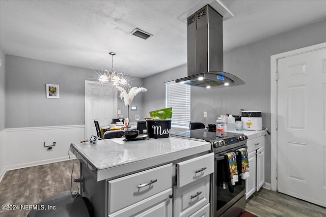 kitchen with decorative light fixtures, wall chimney exhaust hood, dark wood-type flooring, stainless steel range with electric cooktop, and an inviting chandelier