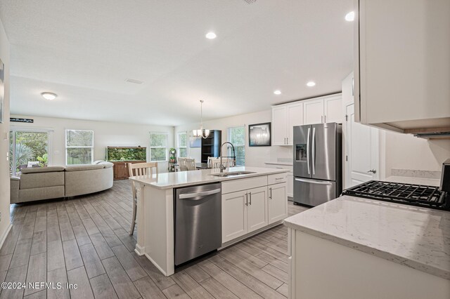 kitchen featuring an island with sink, sink, white cabinetry, stainless steel appliances, and light wood-type flooring