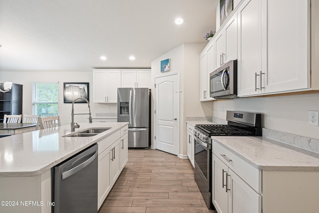 kitchen with light wood-type flooring, white cabinets, a center island with sink, appliances with stainless steel finishes, and light stone countertops