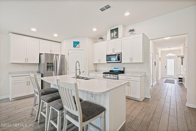 kitchen featuring light hardwood / wood-style floors, an island with sink, white cabinets, stainless steel appliances, and sink