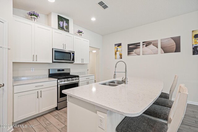 kitchen featuring light hardwood / wood-style flooring, appliances with stainless steel finishes, a kitchen island with sink, and a breakfast bar area