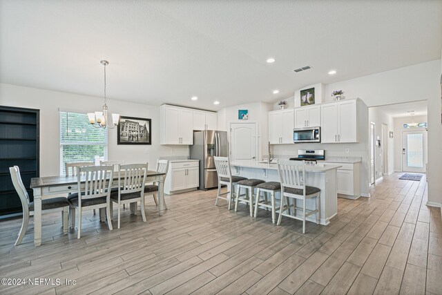 kitchen featuring hanging light fixtures, a kitchen island with sink, a chandelier, white cabinetry, and stainless steel appliances