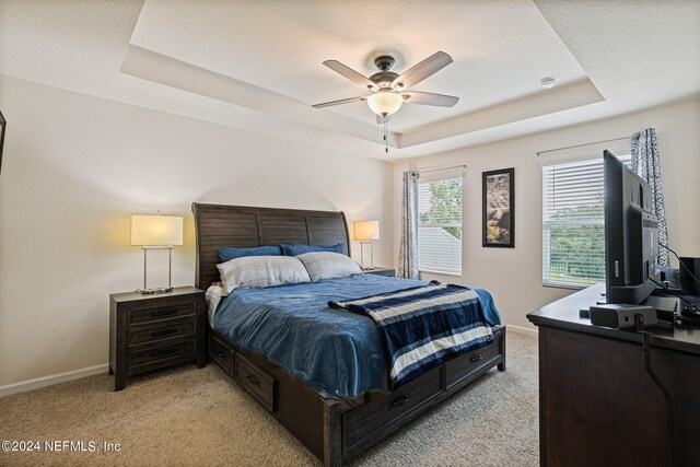 bedroom with light carpet, a tray ceiling, ceiling fan, and a textured ceiling