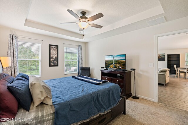 bedroom with light wood-type flooring, a textured ceiling, a tray ceiling, and ceiling fan