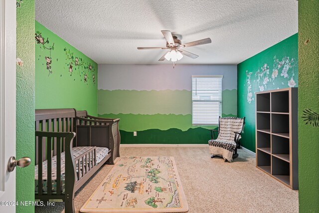 carpeted bedroom with a crib, a textured ceiling, and ceiling fan