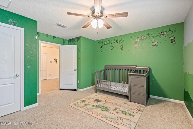 bedroom featuring a crib, a textured ceiling, carpet, and ceiling fan