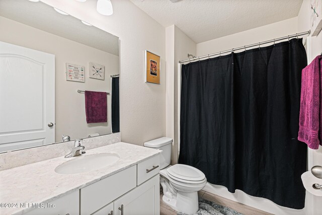 bathroom with a textured ceiling, curtained shower, vanity, and toilet