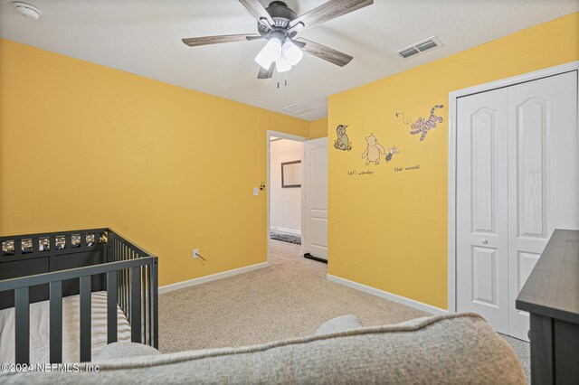 bedroom with a closet, ceiling fan, a nursery area, and carpet floors