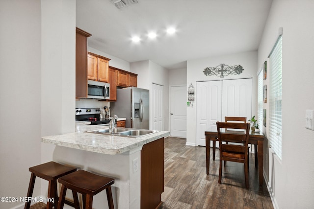 kitchen featuring a breakfast bar area, sink, kitchen peninsula, appliances with stainless steel finishes, and dark hardwood / wood-style flooring