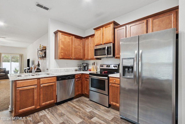 kitchen featuring stainless steel appliances, wood-type flooring, kitchen peninsula, and sink