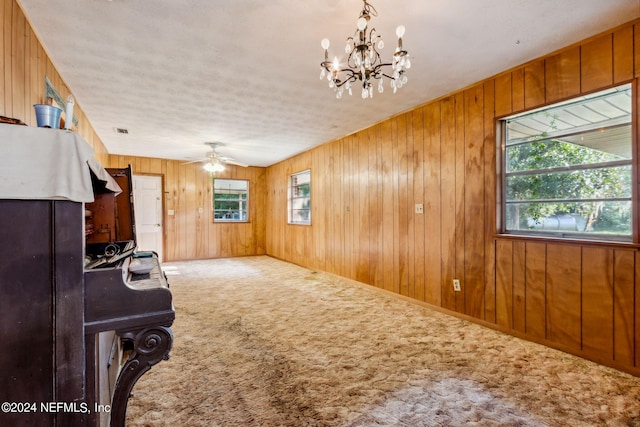 interior space with ceiling fan with notable chandelier, wood walls, carpet, and a wealth of natural light