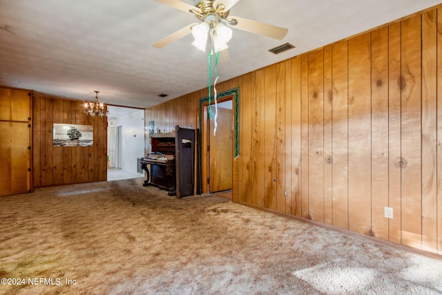 unfurnished living room featuring carpet floors, ceiling fan with notable chandelier, and wood walls