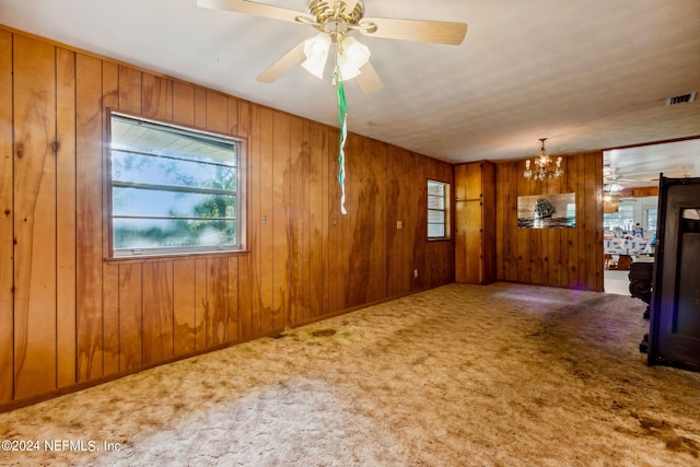 unfurnished living room featuring wooden walls, ceiling fan with notable chandelier, and carpet flooring