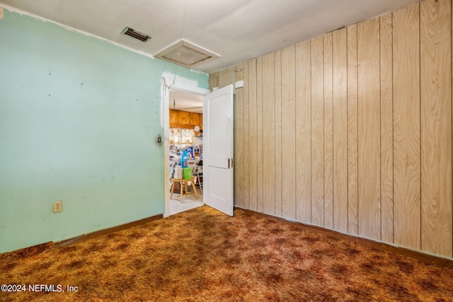 carpeted empty room featuring wooden walls