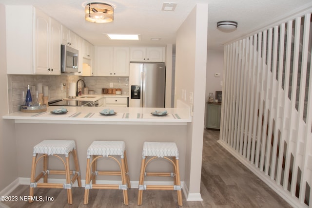 kitchen with white cabinetry, stainless steel appliances, tasteful backsplash, dark hardwood / wood-style flooring, and kitchen peninsula