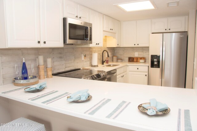 kitchen with sink, kitchen peninsula, white cabinets, and appliances with stainless steel finishes