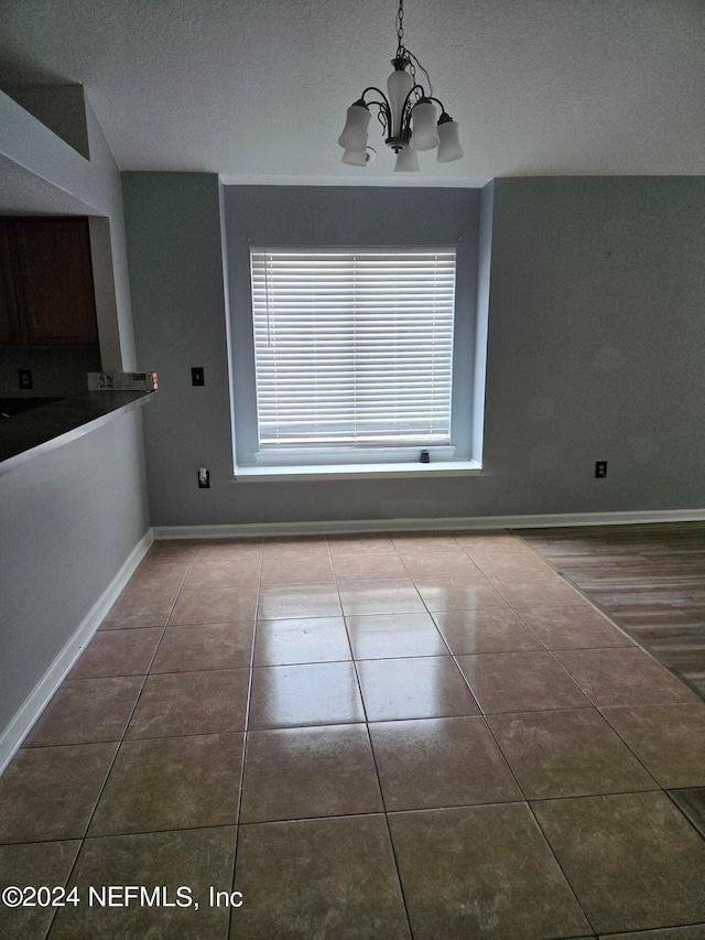 unfurnished dining area featuring a textured ceiling, tile patterned flooring, and a chandelier