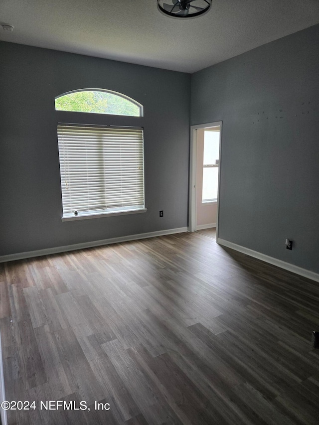 empty room with a textured ceiling, a healthy amount of sunlight, and dark wood-type flooring