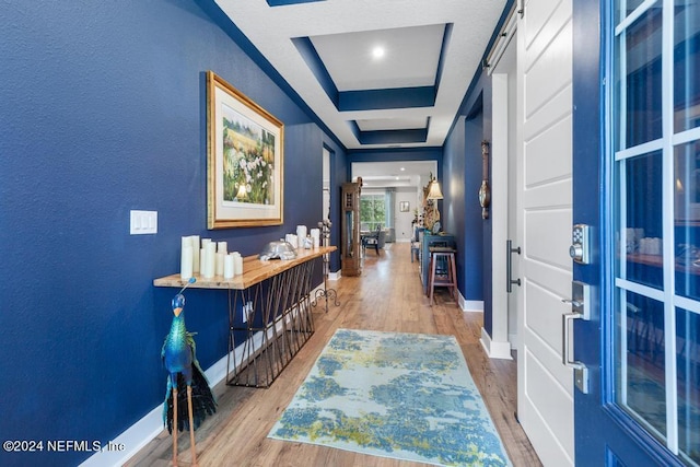 hall featuring wood-type flooring, a tray ceiling, and a barn door