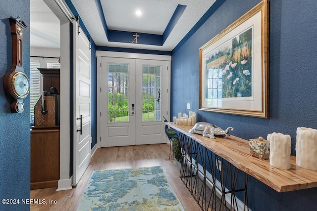 foyer with light hardwood / wood-style flooring, a raised ceiling, french doors, and a barn door