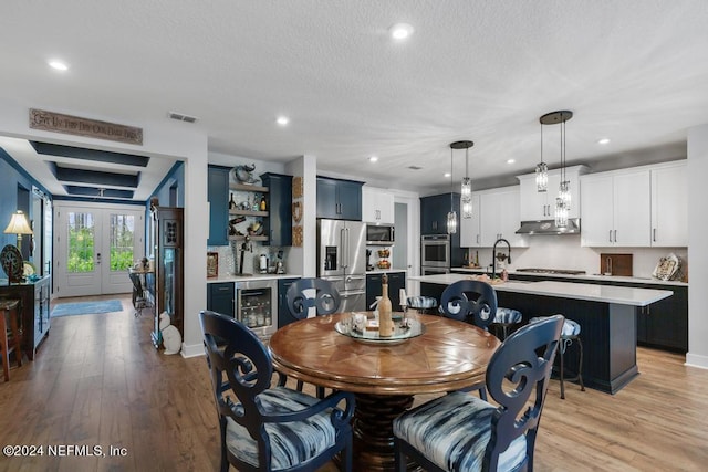 dining room with wine cooler, sink, french doors, a textured ceiling, and light hardwood / wood-style floors