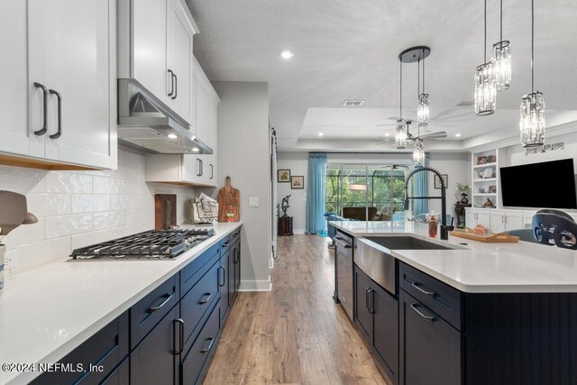 kitchen with white cabinets, pendant lighting, light hardwood / wood-style flooring, a center island with sink, and sink