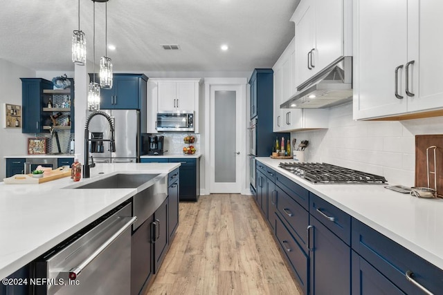 kitchen with appliances with stainless steel finishes, blue cabinets, light hardwood / wood-style floors, white cabinets, and extractor fan