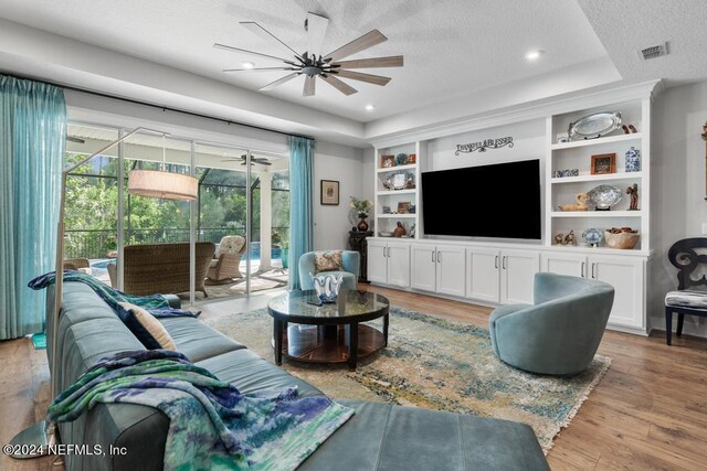 living room featuring light hardwood / wood-style flooring, built in shelves, ceiling fan, and a textured ceiling