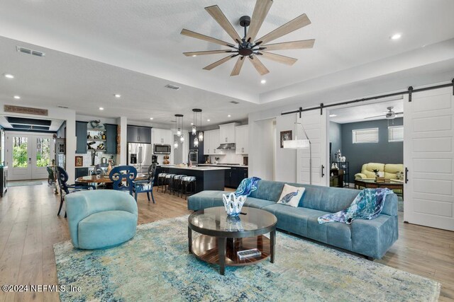 living room featuring light hardwood / wood-style flooring, ceiling fan, and a barn door